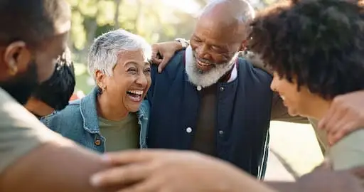 A group of older adults hugging and working on stress management for seniors in a supportive senior living community.