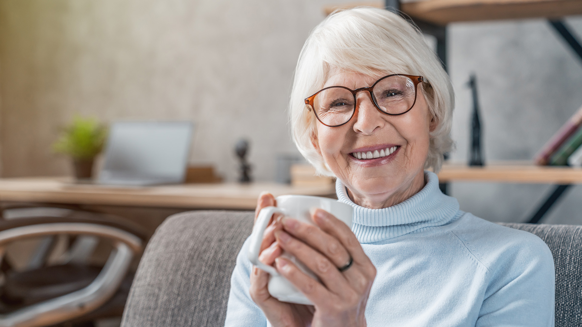 senior woman smiling and holding a coffee cup on the couch